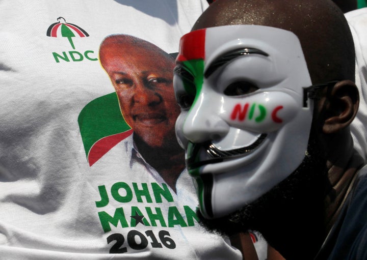 A masked supporter stands next to a picture of John Dramani Mahama, Ghana's president and National Democratic Congress (NDC) presidential candidate as he parades through a street during a presidential campaign rally in Accra, Ghana