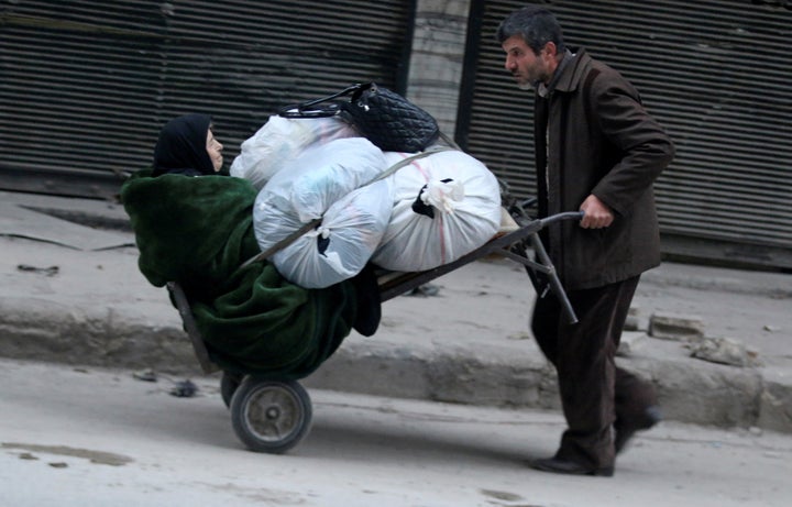A man pushes a cart carrying an elderly woman and belongings as they flee deeper into the remaining rebel-held areas of Alepp
