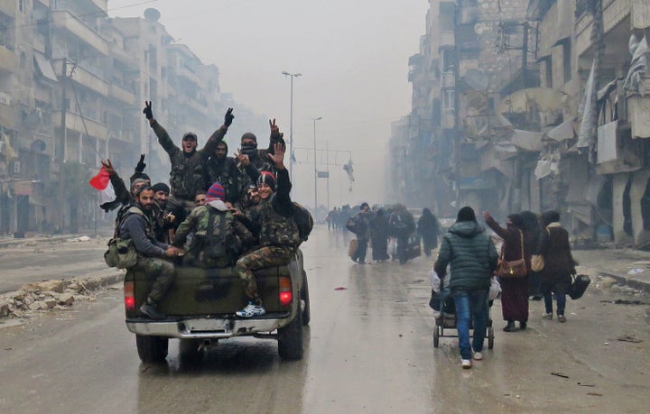 Syrian pro-regime fighters victoriously throw their hands in the air as they drive past residents fleeing violence in the restive Bustan al-Qasr neighborhood on Tuesday, after regime troops retook the area from rebel fighters.