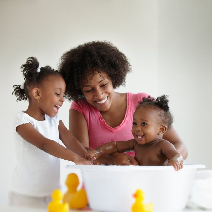 Mother And Daughter Giving Baby Girl A Bath LWA via Getty Images