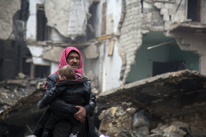 A Syrian man carries a child through the ruins of Aleppo