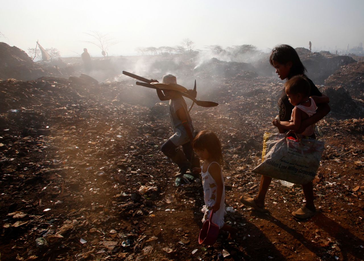 People walk on Smokey Mountain, a small hill made entirely of burnt garbage, in a slum area near Manila