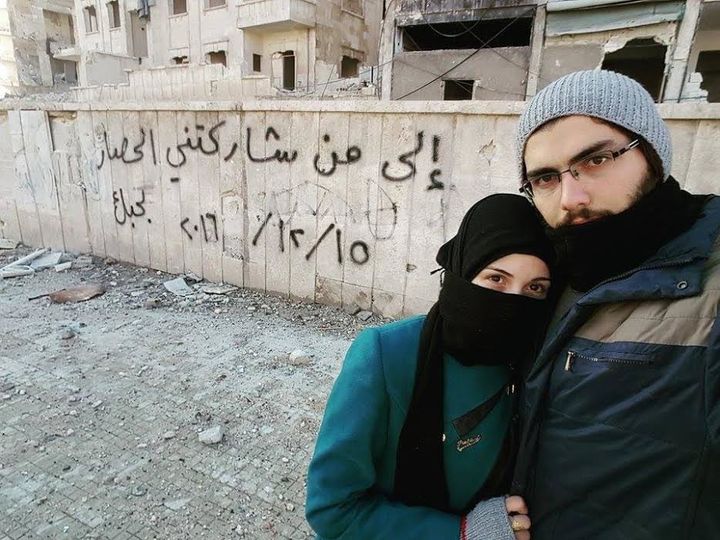 Marwa and Salih pose in front of a graffiti message they left in Aleppo.