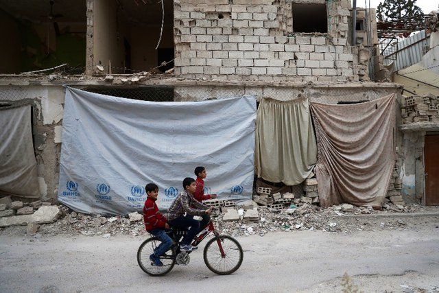 Syrian children ride a bicycle in the rebel-held town of Douma on the eastern outskirts of the capital Damascus on November 13, 2016. Douma, the largest town in the Eastern Ghouta area, with more than 100,000 residents, is surrounded and regularly shelled by regime forces.
