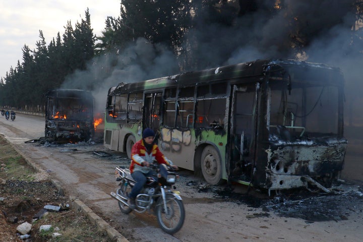 A man on a motorcycle drives past burning buses while en route to evacuate ill and injured people in Idlib province, Syria December 18, 2016