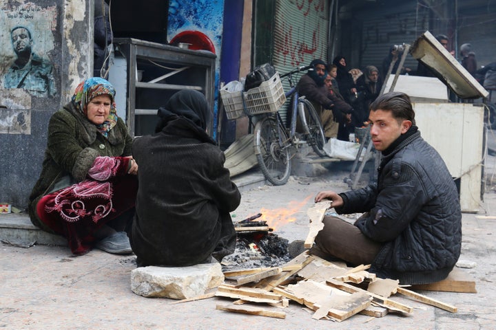 People warm themselves around a fire while waiting to be evacuated from a rebel-held sector of eastern Aleppo, Syria December