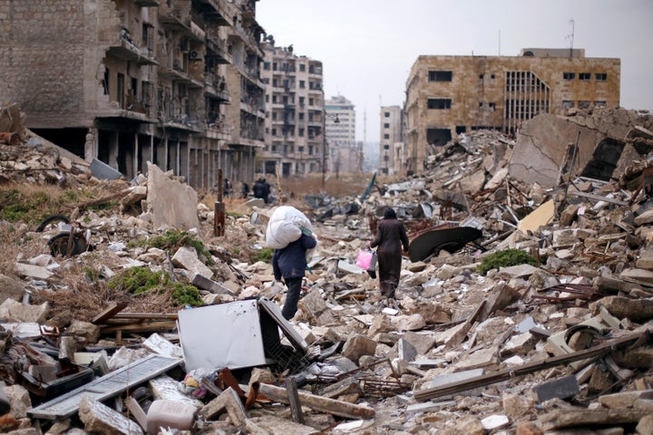 People walk amid the rubble as they carry belongings that they collected from their houses in the government controlled area