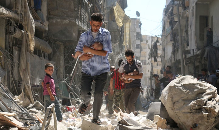 Syrian men carrying babies make their way through the rubble of destroyed buildings.