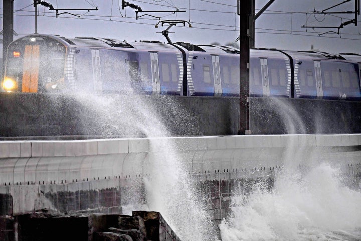 A Scotrail train passes waves crashing against the new weather defences at Saltcoats today