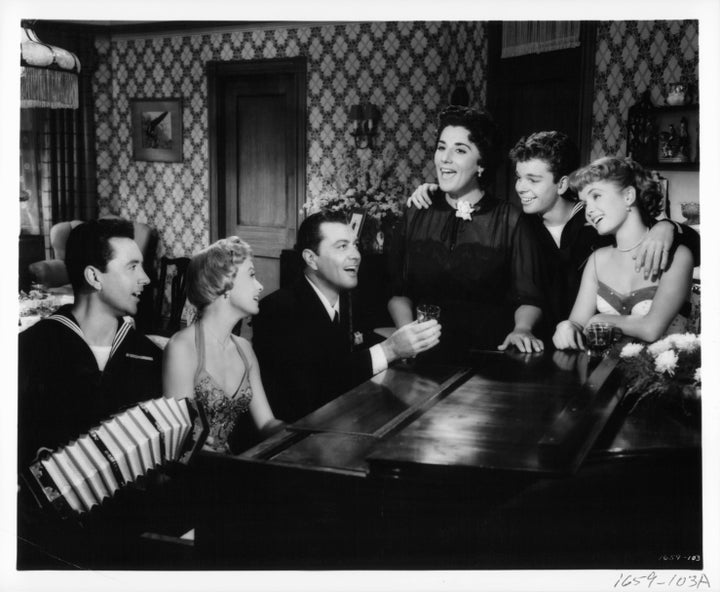 Vic Damone, Jane Powell, Tony Martin, Kay Armen, Russ Tamblyn and Debbie Reynolds gathered around a piano singing in a scene from the film "Hit The Deck."