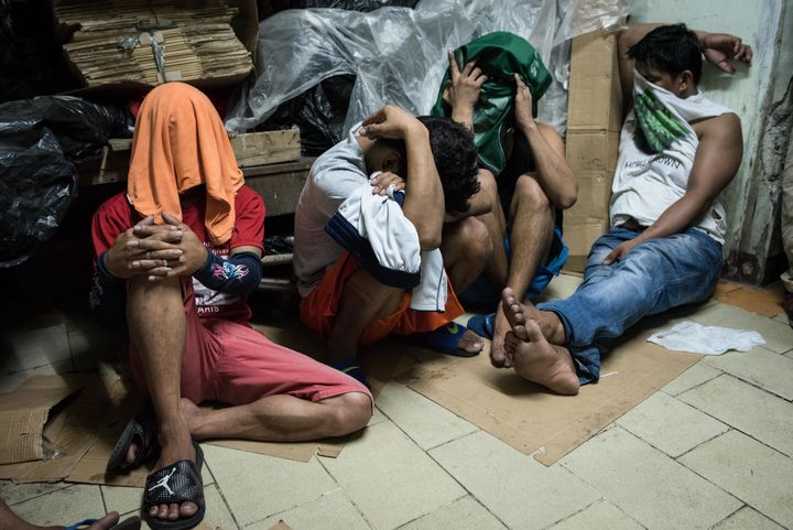 Alleged drug suspects cover their faces during a drug raid on in Manila