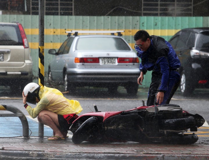 A citizen squats down and hugs an electric line pole beside a motorcycle blown down by Typhoon Soudelor on August 8, 2015 in