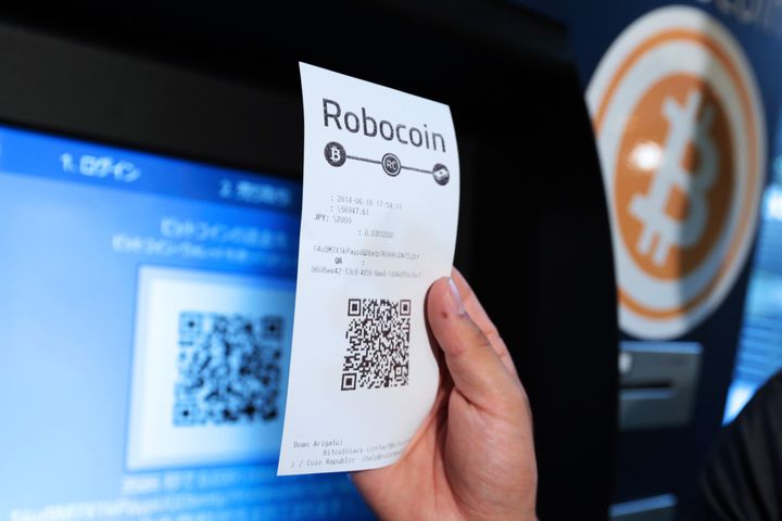 Eugene Aono, a spokesperson for BMEX bitcoin exchange, holds a receipt displaying a quick response (QR) code for a photograph while demonstrating usage of the company's Robocoin-branded automated teller machine (ATM) at The Pink Cow restaurant and bar in Tokyo, Japan, on Wednesday, June 18, 2014.