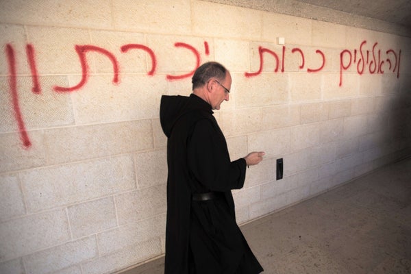 A priest walks past a graffiti reading in Hebrew 'idols will be cast out' as he inspects the damage at the Church of the Mult