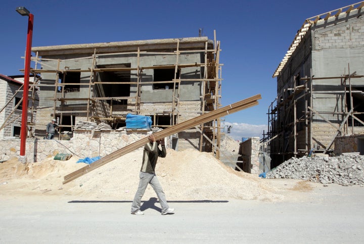 A Palestinian worker carries wood through a construction site in an Israeli settlement in the West Bank on March 13, 2011.