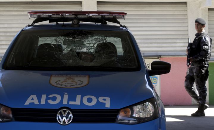 A policeman walks past a police car damaged during a protest at the Mangueira slum in Rio de Janeiro, Brazil August 11, 2015. In the city of Campinas on New Year's Eve, a gunman shot and killed at least 11 people.