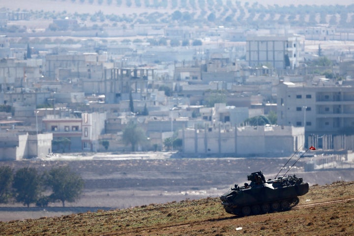 A Turkish army tank drives downhill, in front of ruins of the Syrian town of Kobani (seen in the background) near the Mursitpinar border crossing.