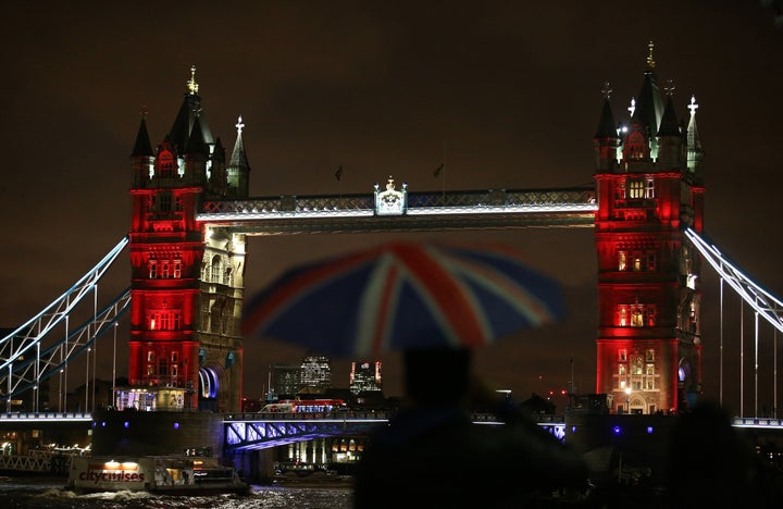 A man shelters from the rain beneath a Union flag-themed umbrella as he photographs London's iconic Tower Bridge, illuminated