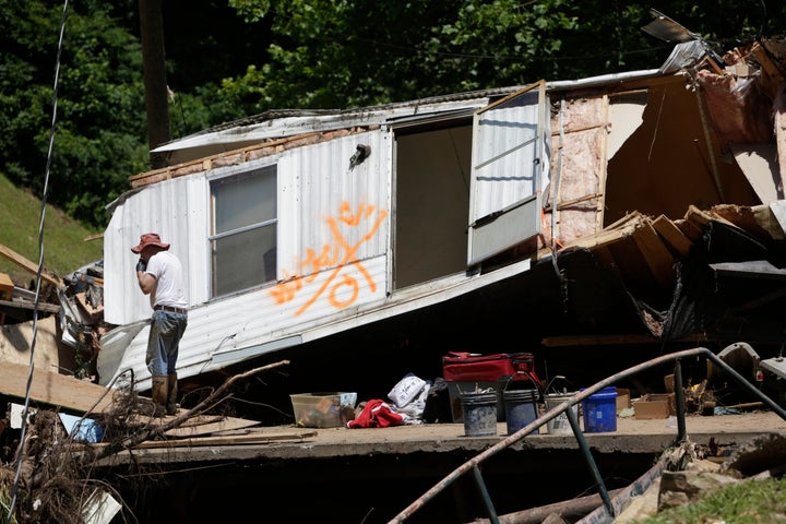 Maynard Tanner, 65, eats a snack on a damaged bridge as part of a mobile home that floated down Jordan Creek rests behind him