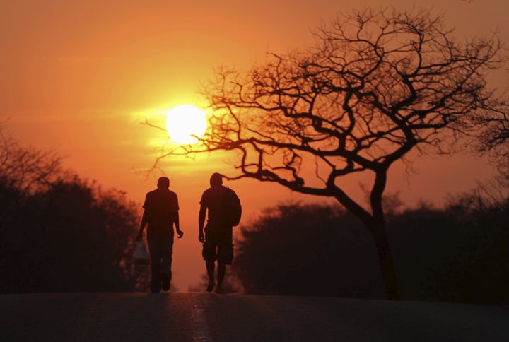 Two men are silhouetted as they walk towards the setting sun inside Hwange national park, September 27, 2015.