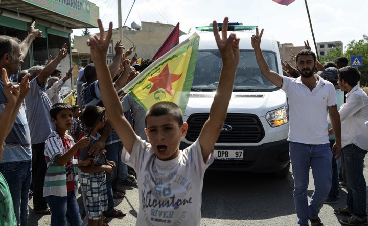 Kurdish people show v-signs and chant slogans along the road as the convoy carrying the body of US citizen Keith Broomfield killed in fighting with militants of the Islamic State.