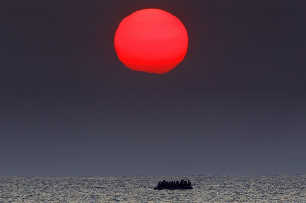 A red sun is seen over a dinghy overcrowded with Syrian refugees drifting in the Aegean sea between Turkey...