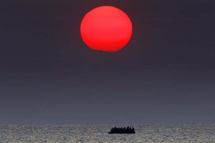 A red sun is seen over a dinghy overcrowded with Syrian refugees drifting in the Aegean sea between Turkey and Greece after its motor broke down off the Greek island of Kos, August 11, 2015.