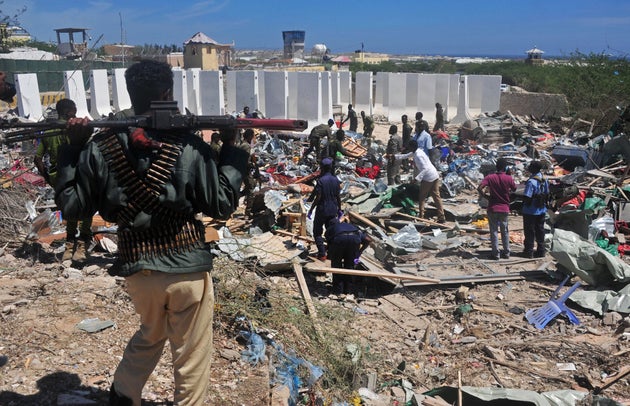 Civilians and soldiers stand amongst scattered objects and belongings at the scene of a car bomb attack...