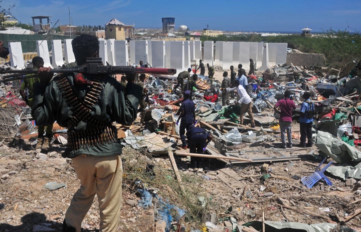 Civilians and soldiers stand amongst scattered objects and belongings at the scene of a car bomb attack near the Peace Hotel of the capital Mogadishu, on January 2, 2017.