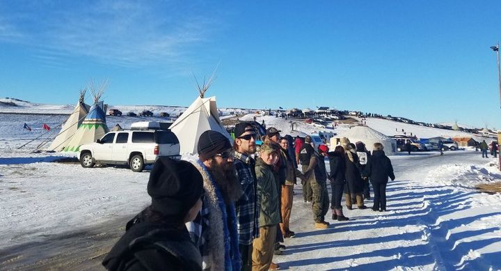 (Left-Right beginning with 1st male) Brandon Trump, Dexter McLelland, and Lachlan Ross. (Background) Tristi Finkbeiner in red hat; during a camp wide prayer circle at Camp Oceti Sakowin. 