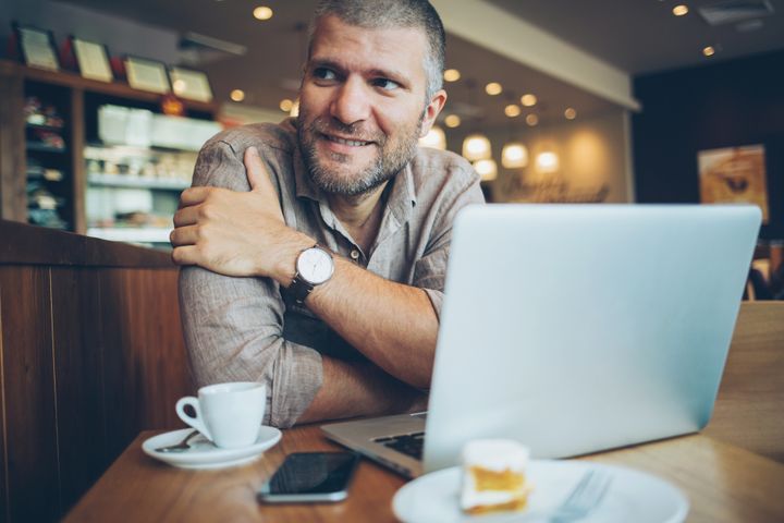 Smiling man having coffee and dessert in a restaurant, with his laptop and smart phone in front of him. pixelfit via Getty Images