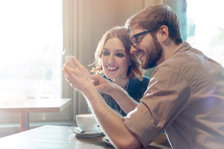 Couple using cell phone in sunny cafe Milton Brown via Getty Images