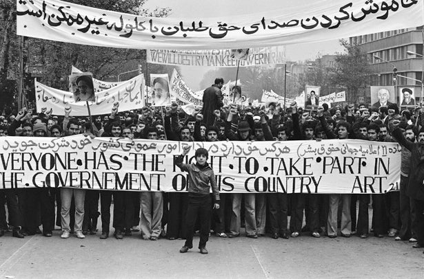 <em>A young Iranian boy raises his fist in front of a poster that reads, "Everyone has the right to take part in the gov