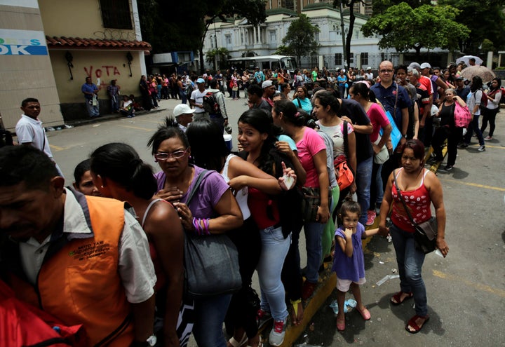 Venezuelans stand in line as they wait to buy essential items and basic food outside of a supermarket in Caracas, Venezuela o