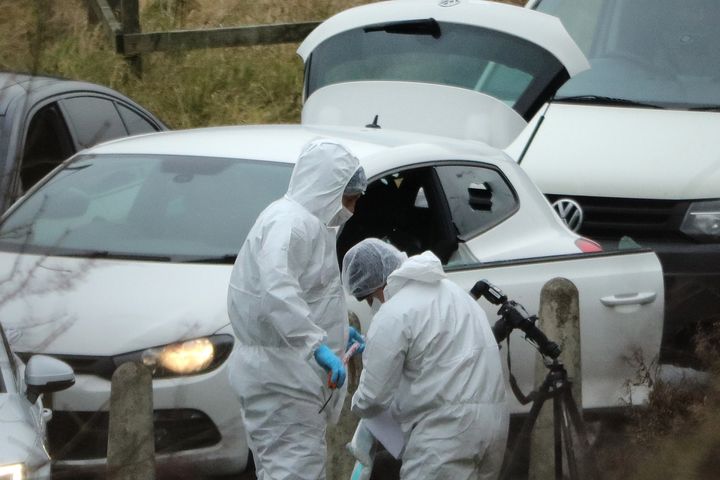 Police forensics officers examine a silver Audi with bullet holes in its windscreen near junction J24 of the M62 where a man died in a police operation.