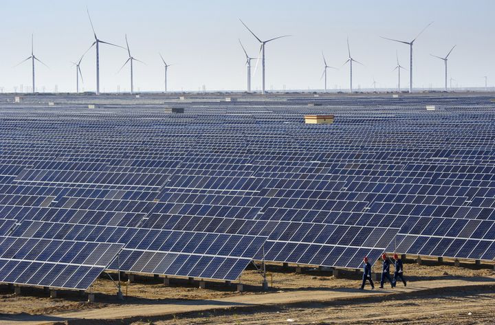 Workers walk past solar panels and wind turbines at a power plant in Hami, Xinjiang Uighur Autonomous Region, China.