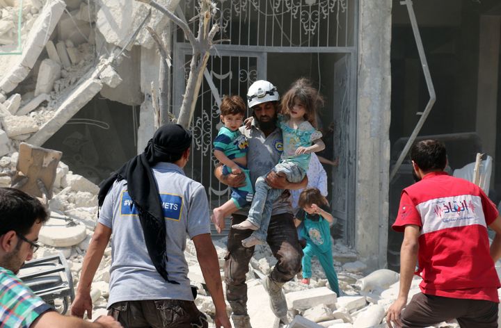 A Syrian rescue worker carries children in the Maadi district of eastern Aleppo after regime aircraft reportedly dropped explosive-packed barrel bombs on Aug. 27, 2016.