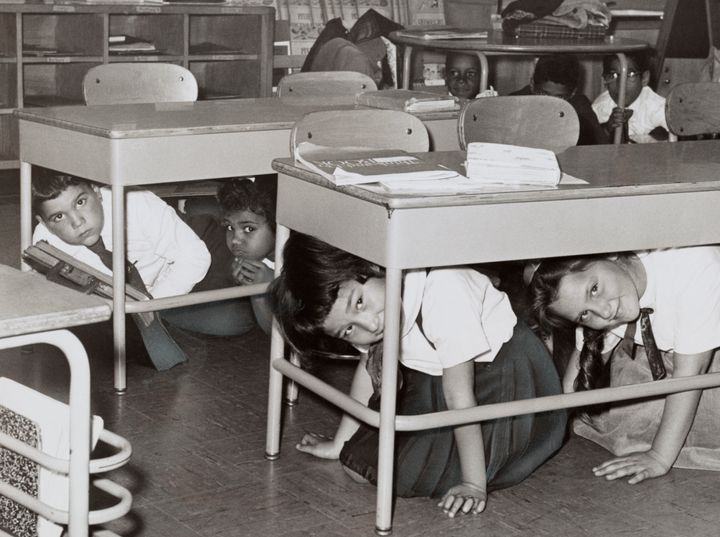 Students at a Brooklyn middle school have a 'duck and cover' practice drill in preparation for a nuclear attack; silver print, 1962.