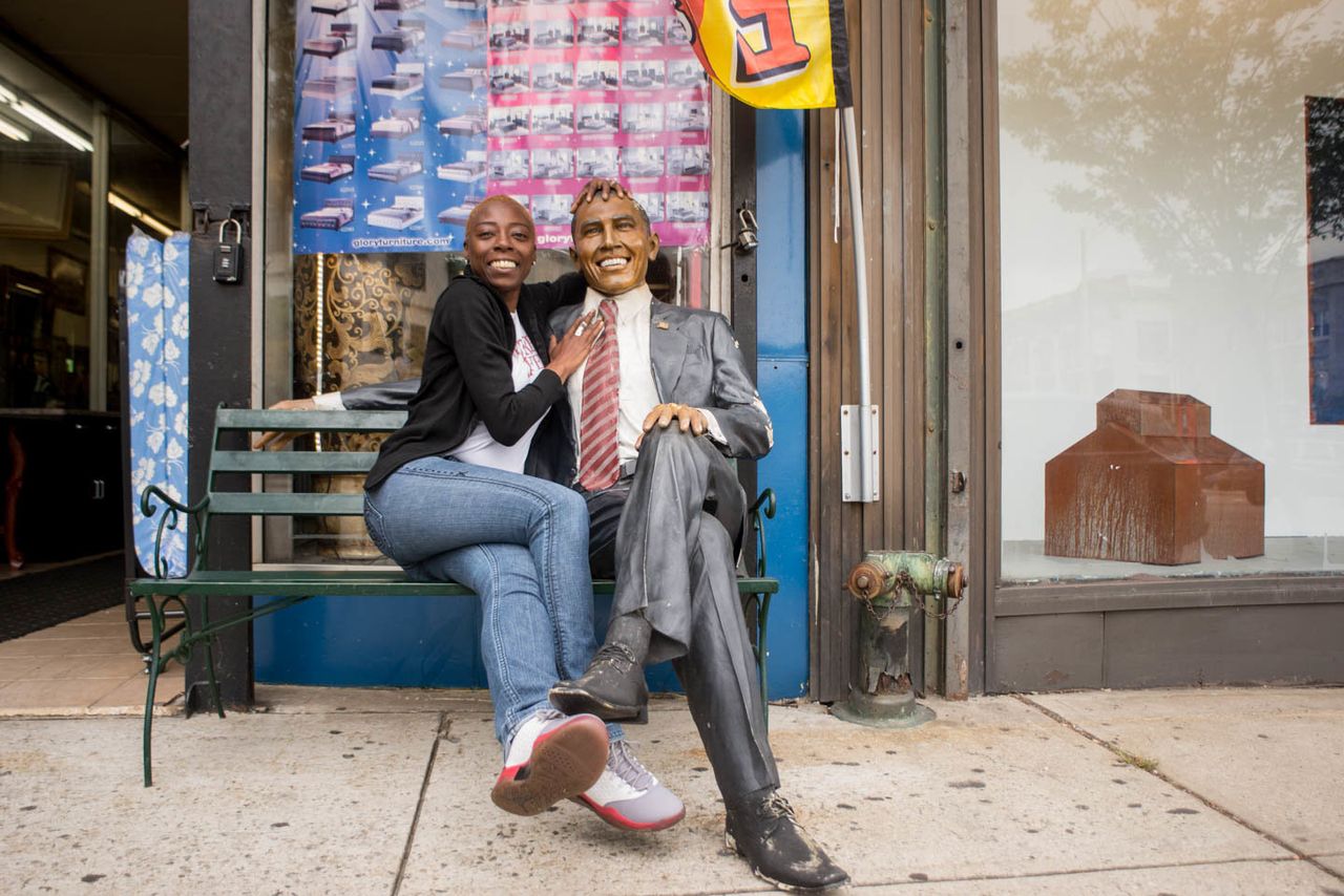A woman with a statue of Obama in front of furniture store Le Moda, 81 Market Street, Newark, New Jersey, 2016.