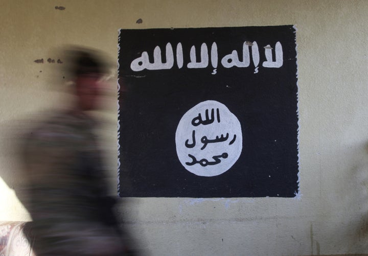 A member of the Iraqi rapid response forces walks past a wall painted with the black flag commonly used by Islamic State militants.