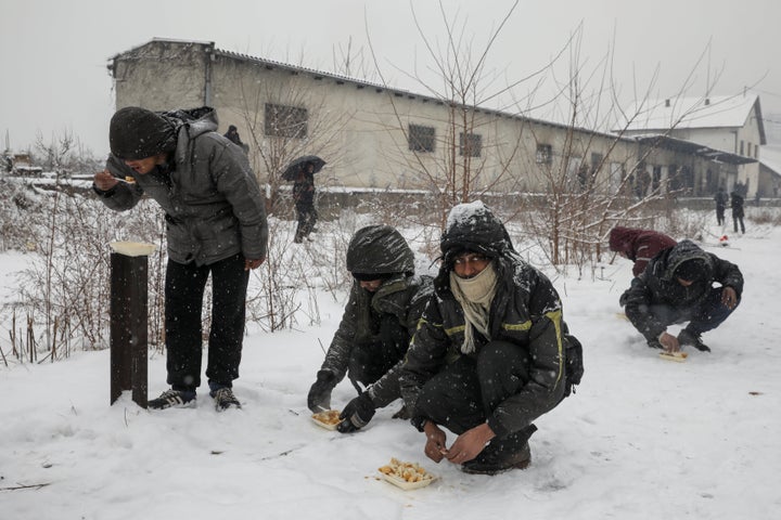 Migrants eat free food during a snowfall outside a derelict customs warehouse in Belgrade, Serbia January 9, 2017.