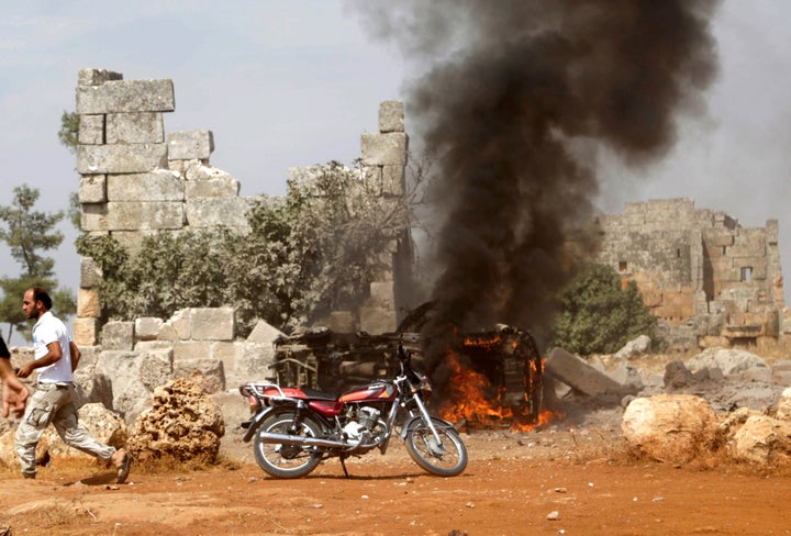 A man runs past a burning military vehicle at a base controlled by rebel fighters from the Ahrar al-Sham Movement, that was t