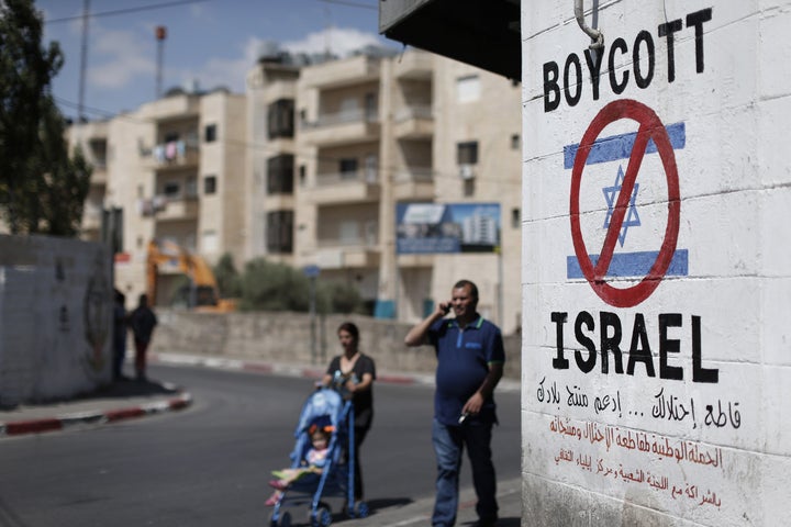 Palestinians walk past a sign painted on a wall in the West Bank town of Bethlehem calling to boycott Israeli products coming