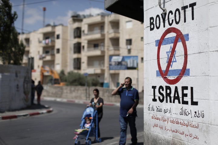 Palestinians walk past a sign painted on a wall in the West Bank town of Bethlehem calling to boycott Israeli products coming from Jewish settlements.