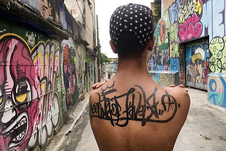 Aquilas Mano Costa from Rio De Janeiro. Mr. Costa a community coordinator and a tattoo artist displays his Meeting Of Favela tattoo. Aquilas is a member of the Costa family which was the host family of Ms. Cooper and other guests durin MOF. Meeting Of Favela 2016. Favela Operaria. Duque de Caxias. Rio De Janeiro, Brazil. 