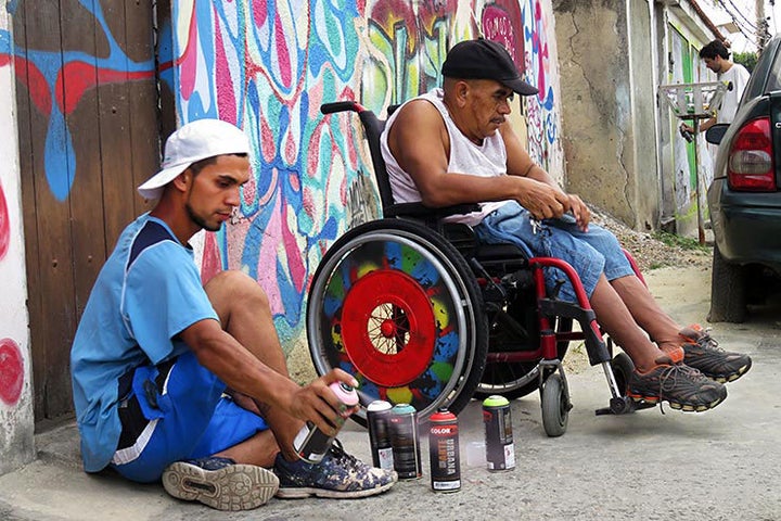 An unidentified artist paints the wheels of a wheel chair. Meeting Of Favela 2016. Favela Operaria. Duque de Caxias. Rio De Janeiro, Brazil. 