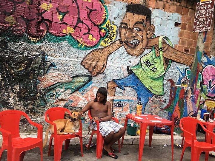 <p>Sergio with his dog Thor. In the background a mural painted by Talu for last year’s MOF. Meeting Of Favela 2016. Favela Operaria. Duque de Caxias. Rio De Janeiro, Brazil. </p>