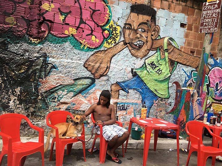 Sergio with his dog Thor. In the background a mural painted by Talu for last year’s MOF. Meeting Of Favela 2016. Favela Operaria. Duque de Caxias. Rio De Janeiro, Brazil. 