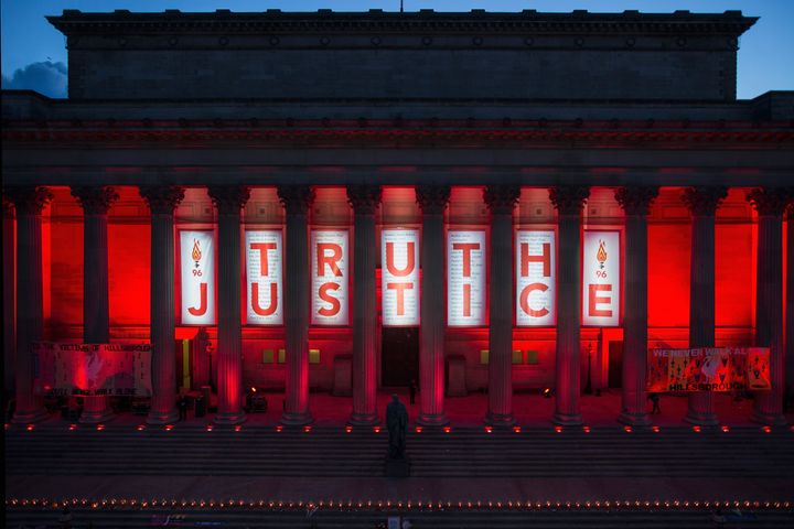A banner is hung from Liverpool's Saint George's Hall and illuminated in red after a vigil for the 96 victims
