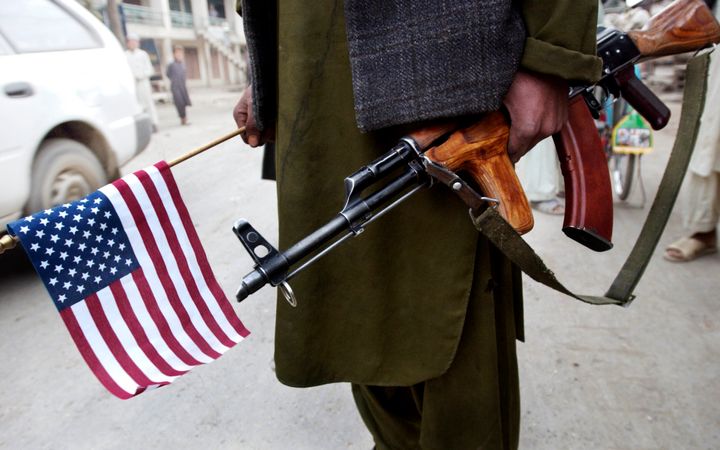 A soldier in Afghanistan holds a U.S. flag and a Kalishnikov rifle.